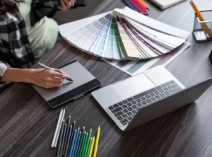 Diseñador gráfico trabajando en la creación de un logotipo con paletas de color, tableta digital y portátil sobre escritori