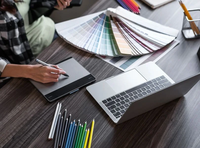 Diseñador gráfico trabajando en la creación de un logotipo con paletas de color, tableta digital y portátil sobre escritori